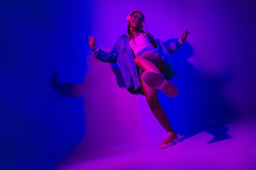 Joyful young woman dancing confidently in vibrant neon lighting, showing energetic movements and a...