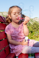 Cute funny little girl toddler child blowing soap bubbles in park summer outside