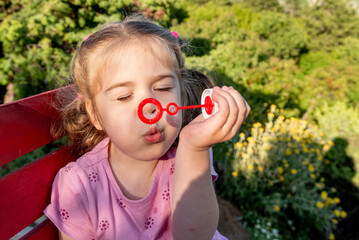 Cute funny little girl toddler child blowing soap bubbles in park summer outside