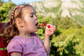 Cute funny little girl toddler child blowing soap bubbles in park summer outside
