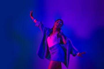 Joyful young woman in denim outfit dancing in vibrant neon lights, embracing a lively party...