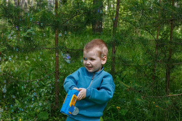 A smiling child holds a bubble gun in his hands while playing in nature. Soap bubbles.