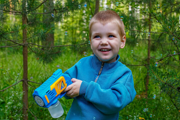 A happy child holds a bubble gun in his hands while playing in nature. Soapy bubbles.