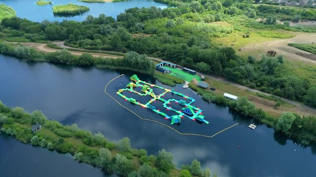 Aerial close up drone shot beautiful blue lakes and lush greenery with inflatable aqua water park play event near Little Paxton England UK