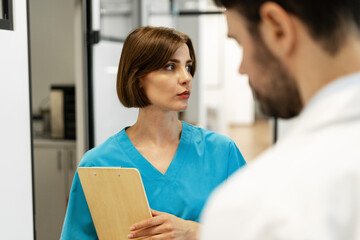 Female doctor holding clipboard talking with colleague in hospital corridor