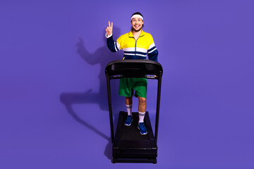 Young athletic man in vibrant retro sportswear exercising on a treadmill and making a peace gesture...