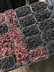 Plastic containers filled with ripe black and red mulberries are arranged on a market stall, viewed from above.