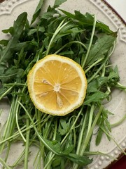 A slice of lemon placed on a bed of fresh arugula leaves served on a ceramic plate, shot from top...