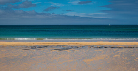 Breaking waves lap a deserted golden sandy beach at Carbis Bay near St Ives on the north coast of Cornwall, UK.  Showing a deep blue sea and dark blue sky. No people.