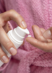Woman in pink bathrobe pumping cream on finger and holding a cosmetic bottle closeup