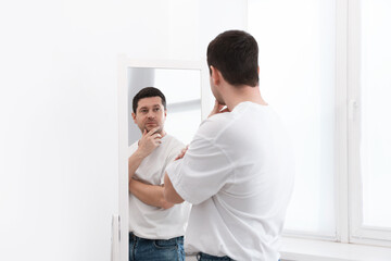 Handsome man looking at himself in mirror indoors