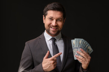 Happy greedy banker pointing at dollar banknotes on black background
