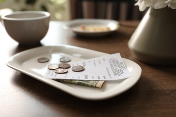 Tips, receipt, dirty plate and cup on wooden table in cafe, closeup