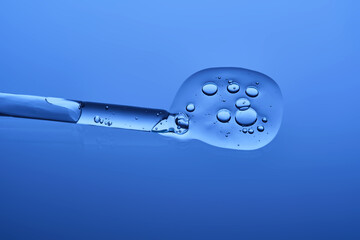 The beautiful texture of the hyaluronic serum with a pipette on a blue background.