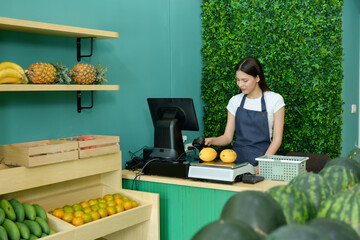 Caucasian female fruit shop owner arranging digital scale with fresh papayas while preparing front...