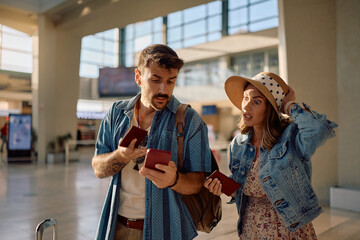 Worried couple checking flight schedule on smart phone at airport.
