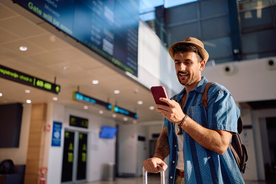 Happy traveler using app on smart phone while waiting for his flight at airport.