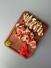 Top-down photo of sushi rolls on a wooden tray with wasabi and ginger on a light grey table...
