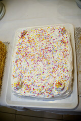 Square birthday cake decorated with colorful crumbs and white whipped cream
