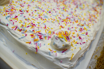 Square birthday cake decorated with colorful crumbs and white whipped cream