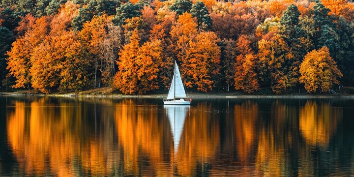 Calm and serene lake with sailboat and fiery tree reflections