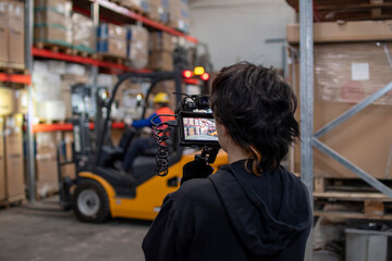 Mujer joven con filmadora y monitor en espacio industrial, desenfoque selectivo