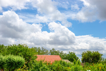 Countryside landscape. view of a house with a red tile roof surrounded by lush green trees under a cloudy blue sky.