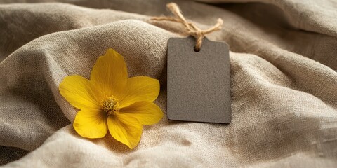 Gentle beige fabric cradles a dark tag with a single yellow blossom
