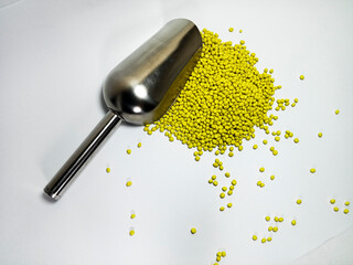 Yellow plastic masterbatch, polymer carries colorful pigments with small scoops poured into a white background, suitable for product catalog design of industrial plastic manufacturing company profiles