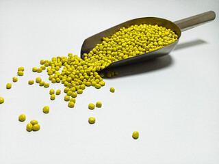 Yellow plastic masterbatch, polymer carries colorful pigments with small scoops poured into a white...