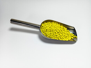 Yellow plastic masterbatch, polymer carries colorful pigments with small scoops poured into a white background, suitable for product catalog design of industrial plastic manufacturing company profiles