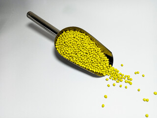 Yellow plastic masterbatch, polymer carries colorful pigments with small scoops poured into a white background, suitable for product catalog design of industrial plastic manufacturing company profiles