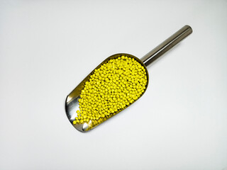 Yellow plastic masterbatch, polymer carries colorful pigments with small scoops poured into a white background, suitable for product catalog design of industrial plastic manufacturing company profiles