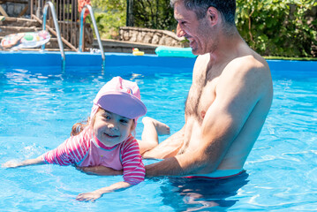 Family Dad and Daughter Swim in Pool on Sunny Day in Summer with Inflatable Ring