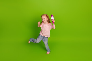 Joyful young girl singing with a colorful microphone, dancing with energy against a vibrant green...