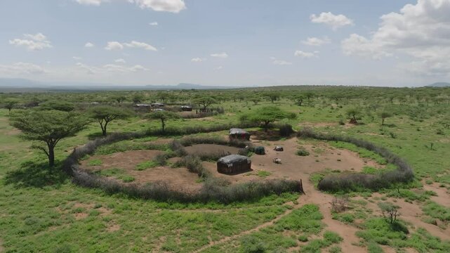 Aerial view of huts encircled by a fence amid a vast landscape with sparse trees and distant mountains, creating a scene of rural simplicity, Sauka, Federal Capital Territory, Nigeria.