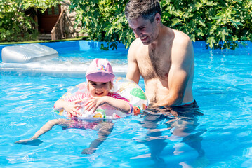 Family Dad and Daughter Swim in Pool on Sunny Day in Summer with Inflatable Ring