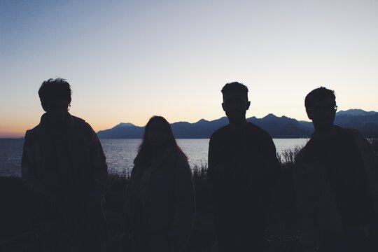 Four young adults silhouettes during sunset over seascape