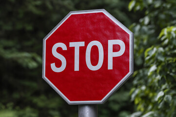 A Photorealistic Closeup of a Red Octagonal Stop Sign Against a Blurred Green Foliage Background the Sign Features Bold White S T O P