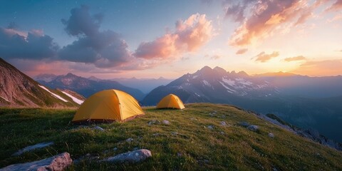 Golden hour light shines on a grassy peak with two yellow tents beneath fading skies and starlit heights