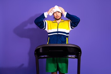 Young man in vintage sportswear exercising on treadmill against a purple background, embodying...