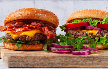 two burgers with beef patty, fried bacon, cheddar cheese, tomatoes, on a light table,