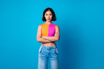 Young stylish woman in casual colorful top and jeans posing confidently against a bright blue...