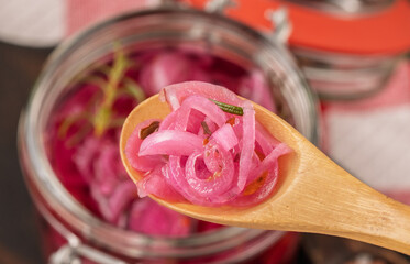 Pickled red onion rings on a wooden spoon on a glass jar. Appetizer, condiment or topping. Healthy fermented food. High quality photo