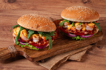 two shrimp burgers and buns with sesame seeds, bacon, lettuce, tomatoes and onions,on a wooden board, rustic style,