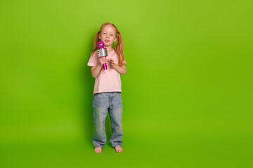 Happy child with a microphone on a green background, expressing joy and creativity while posing in...