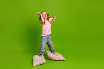 Happy little girl dancing playfully on pillows against a vibrant green background showcasing...