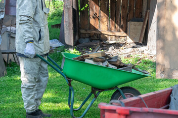 A person is pushing a green wheelbarrow filled with wood debris on a grassy area.