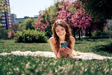Pretty woman relaxing in a sunny park setting while enjoying her smartphone, surrounded by blooming...