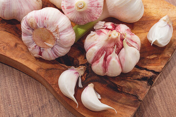 Close-up of several heads and cloves of fresh garlic lying on a wooden chopping board, natural...